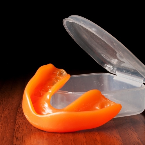 Orange athletic mouthguard next to its clear carrying case
