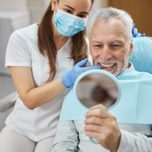 Man smiling while holding dental mirror