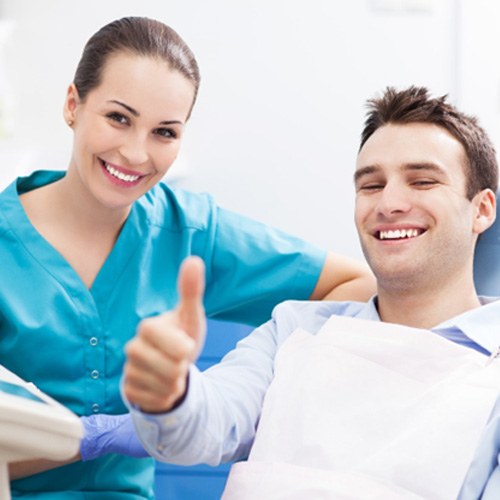 Smiling male patient giving thumbs up with dental assistant 