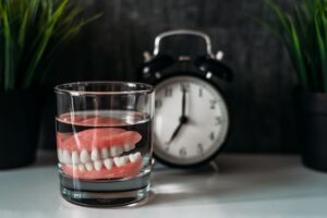 Set of dentures in a glass next to an alarm clock